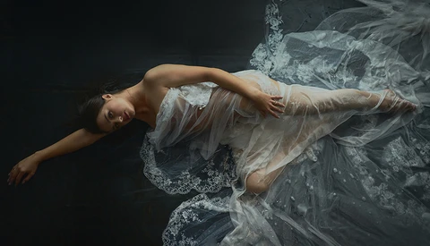 Woman floating horizontally in dark water wearing a translucent white dress with flowing fabric.