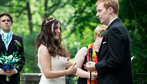 Bride and groom exchanging vows during outdoor wedding ceremony in natural green setting.