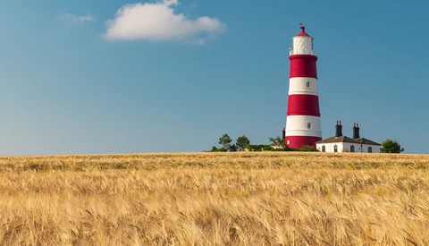 Red and white striped lighthouse standing on a golden grain field under clear blue sky.