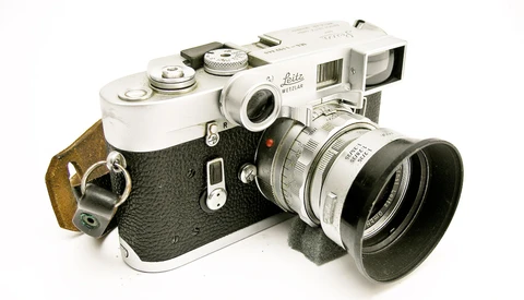 Vintage Leica rangefinder camera with interchangeable lens and brown leather strap.