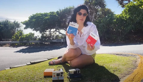 Woman holding vintage cameras and film boxes outdoors in natural daylight.