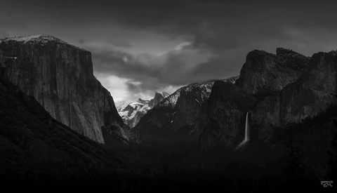 Yosemite Valley framed by towering granite cliffs under dramatic storm clouds with a waterfall visible in the distance.