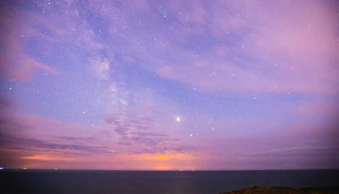 Purple and orange twilight sky with stars visible above a dark horizon and water.