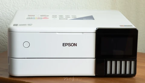 Epson EcoTank printer with white body and black ink tank cartridge module on wooden surface.