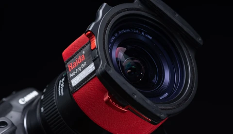 Wide-angle lens with red focus ring mounted on camera body against black background.