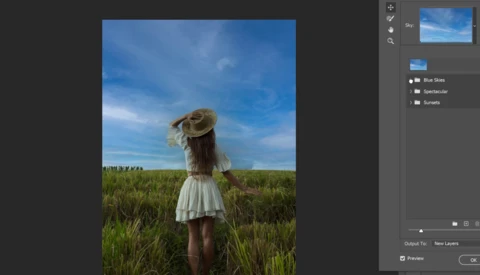 Woman in white dress and straw hat standing in green field under blue sky.