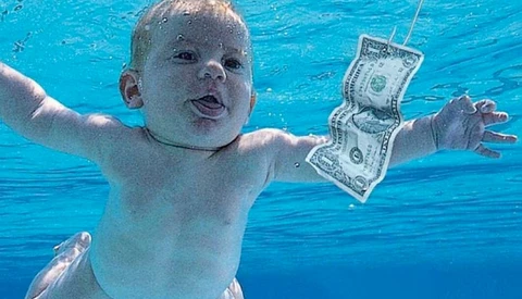 Infant underwater reaching toward floating dollar bills in pool.