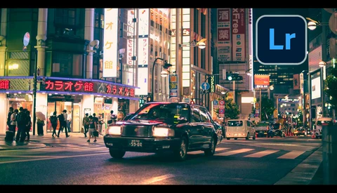 Taxi crossing a busy nighttime intersection in a Japanese city district with neon signs and pedestrians.