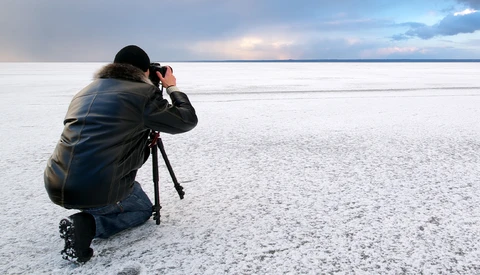 Photographer crouching on a frozen lake, composing a shot with a camera mounted on a tripod.