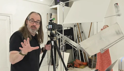Photographer gesturing toward camera mounted on lighting stand in studio setup.