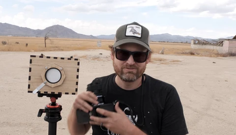 Photographer holding a light meter with a calibration card on a tripod in an arid landscape.