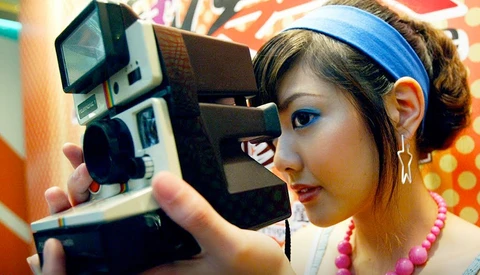 Photographer holding vintage instant film camera to her face against colorful patterned background.