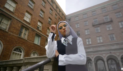 Woman in nun habit and business vest adjusting her headpiece against urban brick buildings.
