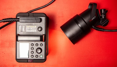 Light meter and spot meter device laid out on bright red surface with cables attached.