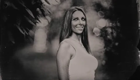 Woman in white tank top smiling over shoulder in black and white portrait.