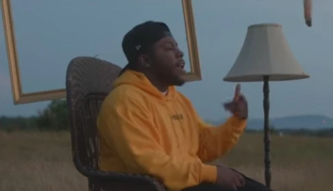 Person in yellow jacket sitting in chair outdoors during golden hour, gesturing while speaking.