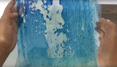 Hands holding a clear resin casting with blue and white swirled patterns and bubble textures.