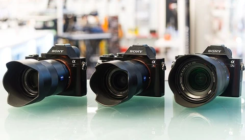 Three Sony Alpha mirrorless cameras with different lenses arranged side by side on a green surface.