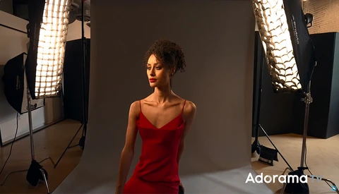 Woman in red dress posed against gray backdrop with professional studio lighting setup.
