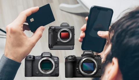 Photographer's hands holding a credit card, smartphone, and three mirrorless camera bodies displayed on a white surface.