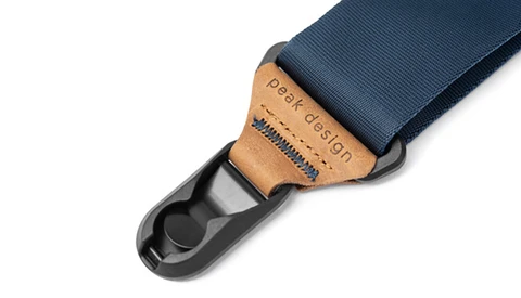 Camera strap with tan leather pad and black plastic attachment hardware against navy blue webbing.