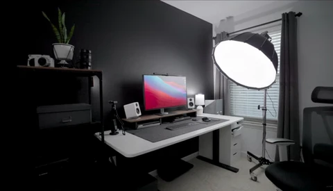 Professional photography studio setup with soft-box lighting, monitor displaying gradient wallpaper, and organized desk workspace.