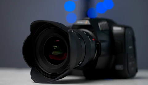 Professional mirrorless camera with wide-angle lens attached, positioned on white surface with blurred blue bokeh lights in background.