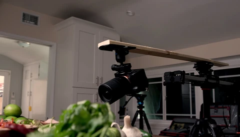 Professional camera mounted on tripod with overhead lighting rig in kitchen studio setup.