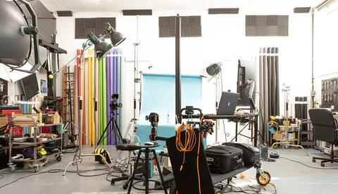 Professional photography studio with lighting rigs, colored backdrop panels, tripods, and production equipment arranged throughout an industrial space.