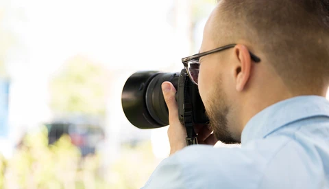 Photographer wearing glasses looking through camera viewfinder while shooting outdoors.