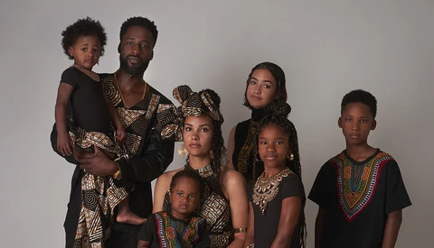 Family of seven posing together wearing coordinated black and patterned clothing against a neutral background.