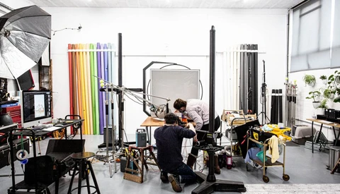Photographer working in a studio with lighting equipment, reflectors, and color swatches on the walls.