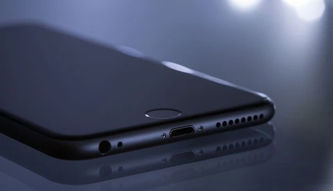 Dark smartphone positioned diagonally on reflective surface with side ports and speaker grille visible.