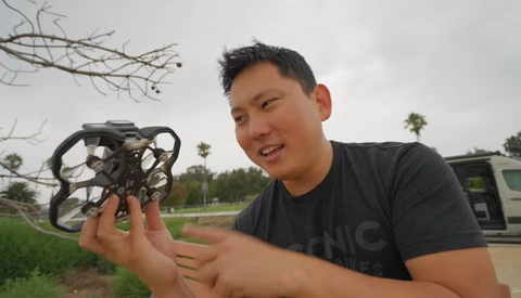 Man holding a small drone with protective cage indoors during daytime.