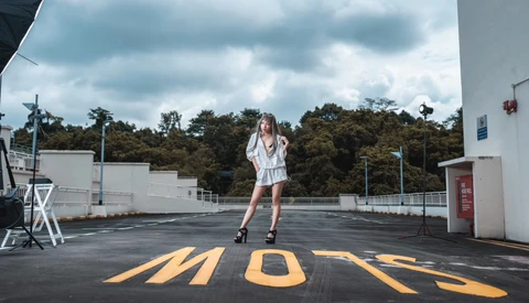 Woman in white shirt posing on rooftop with yellow crosswalk markings painted on asphalt.