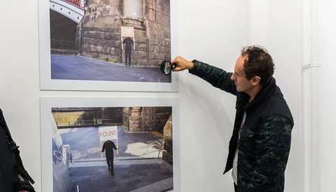 Man pointing at framed photograph on gallery wall during exhibition.