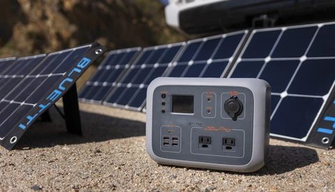 Portable power station with solar panels in sandy outdoor setting.