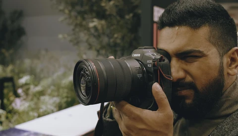 Photographer holding a Canon DSLR with telephoto lens up to his eye while composing a shot.
