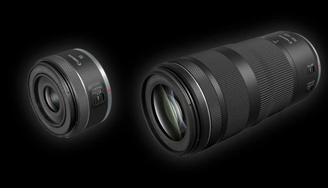 Two black camera lenses displayed against a dark background, showing a compact prime lens on the left and a longer telephoto zoom lens on the right.