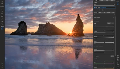 Dramatic sunset over ocean with three towering rock formations silhouetted against golden sky and reflected in wet sand.