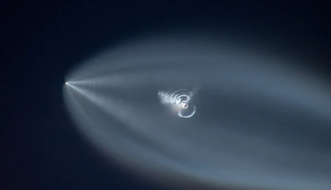 Spiraling blue-white light phenomenon against dark night sky with radiating streaks.