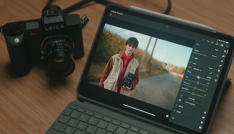 Leica M-series film camera next to tablet displaying portrait editing software with image of person in red jacket.