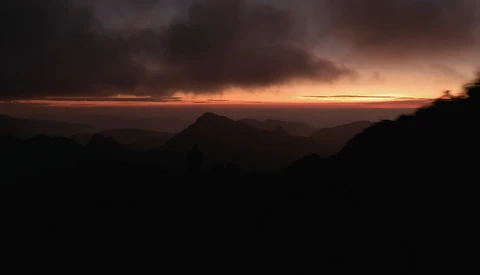 Silhouetted mountain ridges against an orange and gold sunset sky with dramatic clouds.