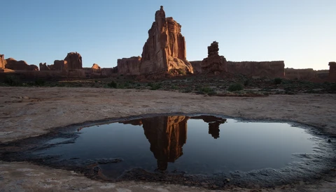 Desert rock formations reflected in a still pool of water at golden hour.