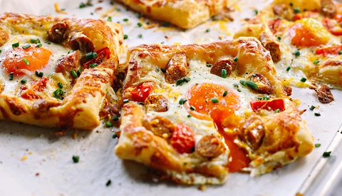 Golden-brown pizza pieces with melted cheese, red peppers, and fresh herbs scattered on white surface.