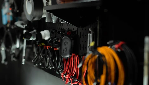 Close-up of a pegboard wall organizer with red and yellow coiled cables and black mounted tools against dark background.
