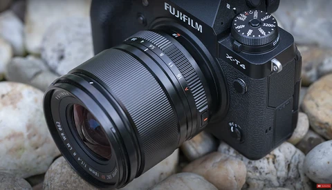 Fujifilm camera with attached lens resting on rocky surface outdoors.