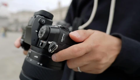 Photographer holding a DSLR camera with telephoto lens attached, wearing a black jacket with striped trim.