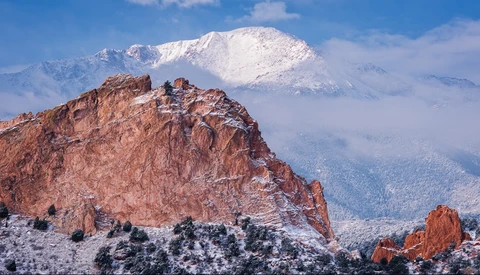Snow-dusted red rock formation with snow-capped mountain peak in distant background under blue sky.
