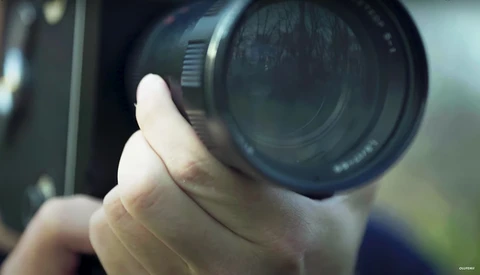 Photographer's hand holding a vintage camera lens in close-up view.